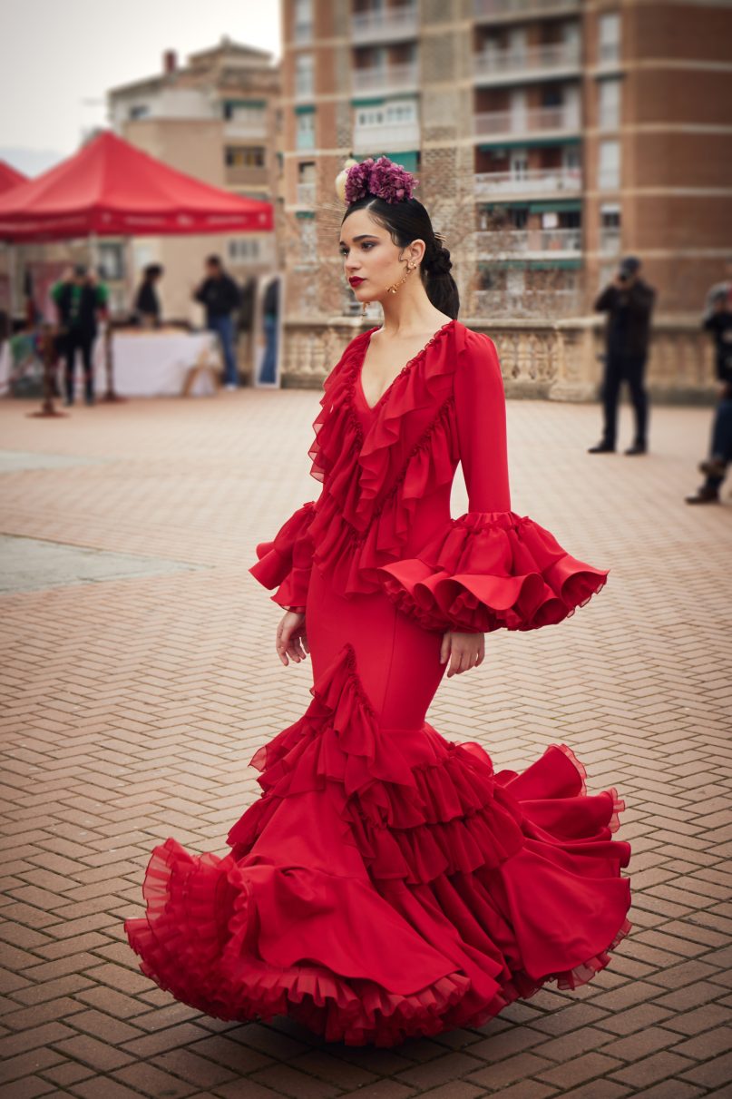 Vestido de flamenca rojo entallado en tejido elástico con manga de doble volantes y detalle de volante en gasa, escote en pico con volantes de gasa, la parte inferior del vestido esta compuesta por volante doble unido y volantes en gasa  y con una gran enagua de rizo en organdí.