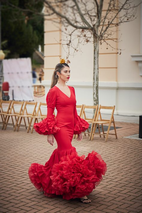 Vestido de flamenca rojo entallado en tejido elástico con manga en detalle copa plisada y un bordado en granate, la parte inferior del vestido esta compuesta por volantes unido en forma canastera  y con una gran enagua de rizo en organdí.