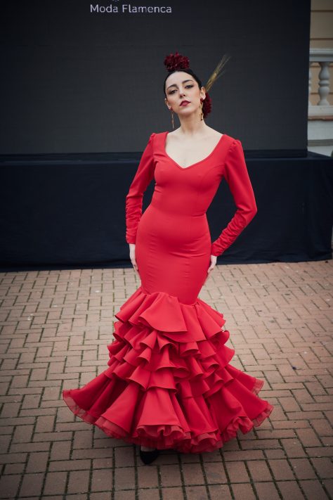 Vestido de flamenca rojo entallado en tejido elástico con manga en detalle rizado y un bordado en granate, la parte inferior del vestido esta compuesta por un conjunto de volantes medianos y uno final grande de gran volumen con organdí con rizo.