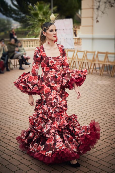 Vestido flamenca de nesgas estampado granate, mangas con volantes y en la parte inferior conjuntos de tres volantes pequeños ademans de una gran volante con mucho volumen y rizos de organdi.