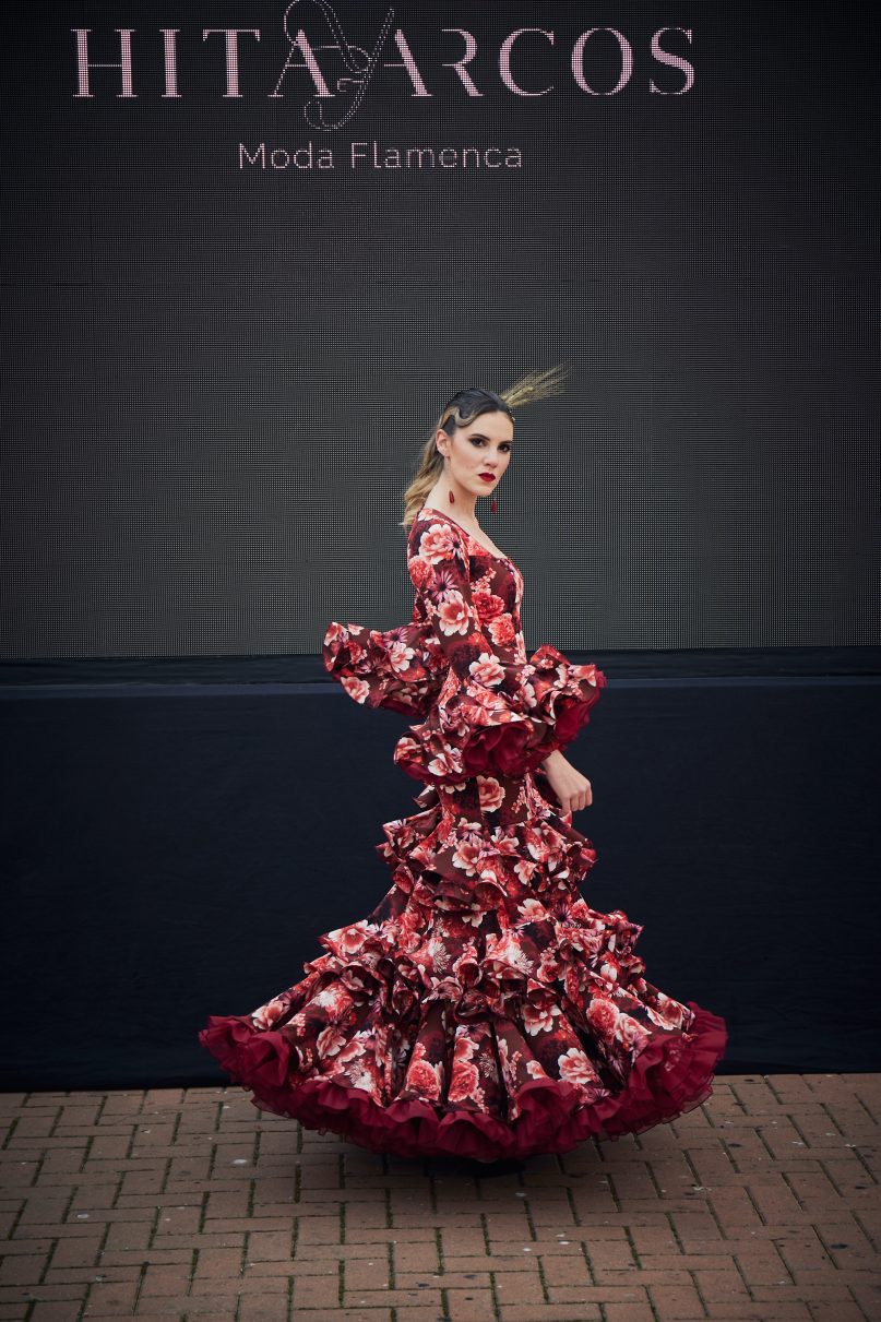 Vestido flamenca de nesgas estampado granate, mangas con volantes y en la parte inferior conjuntos de tres volantes pequeños ademans de una gran volante con mucho volumen y rizos de organdi.