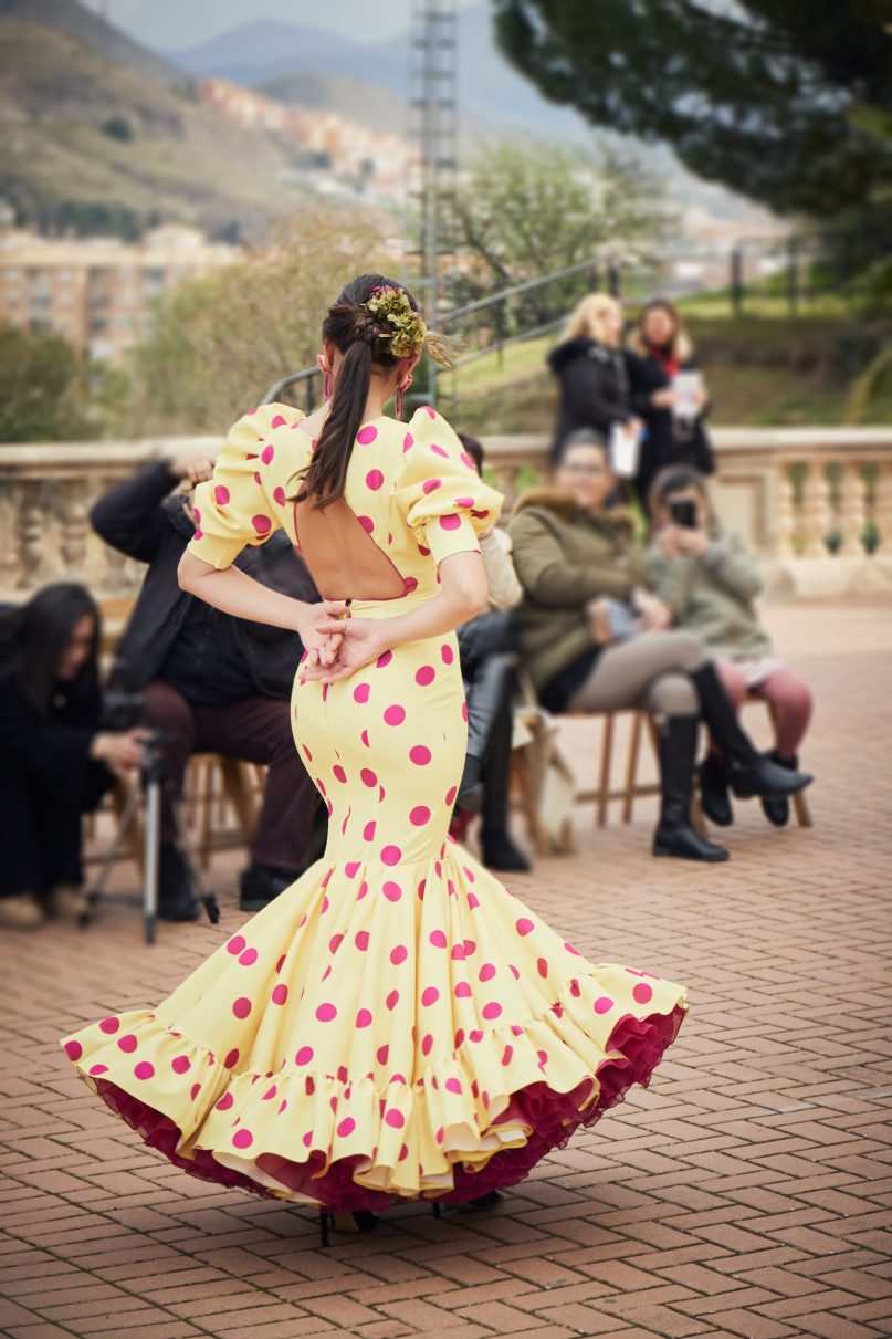 Vestido amarillo con lunar buganvilla, mangas abullonadas, escote cerrado delantero y abierto en forma triangulo trasero. Volantes grande con mucho volumen y enaguas de rizo en buganvilla