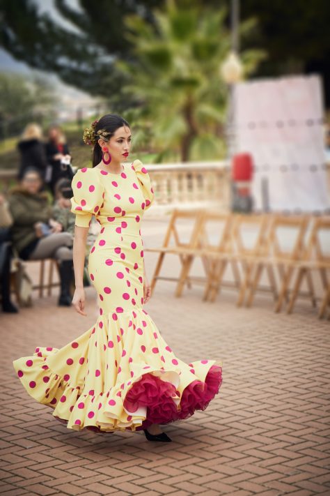 Vestido amarillo con lunar buganvilla, mangas abullonadas, escote cerrado delantero y abierto en forma triangulo trasero. Volantes grande con mucho volumen y enaguas de rizo en buganvilla