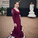 Vestido flamenca de nesgas en color cardenal con bordado de rosa en crudo en ambas mangas en la copa. Es un vestido con dos dobles volantes en la parte inferior uno en color cardenal y el interior en color crudo con lunar negro galleta. El volante superior tiene una subida muy favorecedora en uno de los costados.