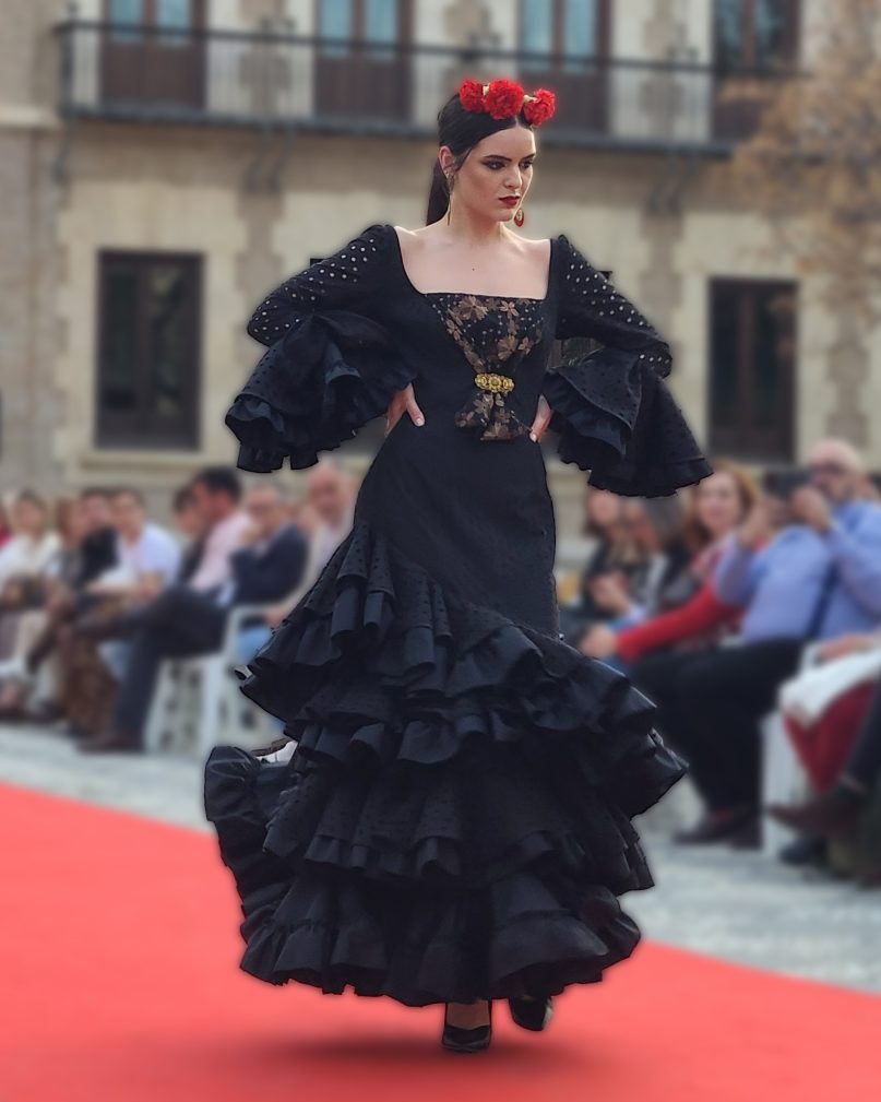 Vestido flamenca en tejido negro perforado con escote delantero y trasero cuadrado y adorno en el delantero, con tres volantes con rizo y manga larga con volante