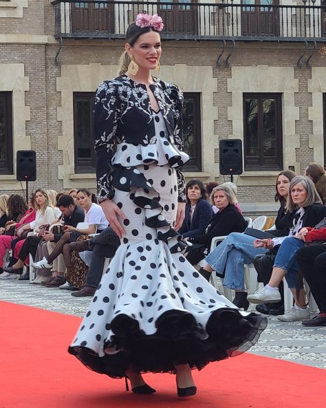 Vestido flamenca gris con lunar en negro, escote corazón con tirante de pasamanería, adorno de volante estilo péplum y con caída sobre la falda, volante grande en el bajo con enagua con vuelo.