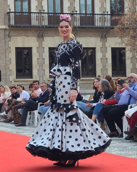 Vestido flamenca gris con lunar en negro, escote corazón con tirante de pasamanería, adorno de volante estilo péplum y con caída sobre la falda, volante grande en el bajo con enagua con vuelo.