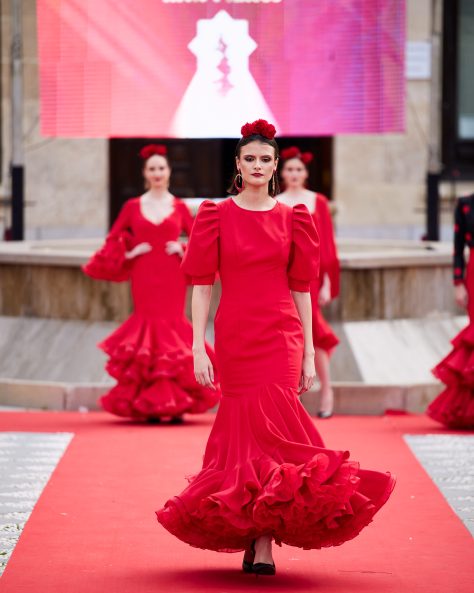 Vestido de flamenca rojo, mangas abullonadas, escote cerrado delantero y abierto en forma triangulo trasero. Volantes grande con mucho volumen y enaguas de rizo en rojo. Detalle encaje en espalda