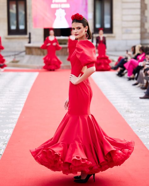 Vestido de flamenca rojo, mangas abullonadas, escote cerrado delantero y abierto en forma triangulo trasero. Volantes grande con mucho volumen y enaguas de rizo en rojo. Detalle encaje en espalda