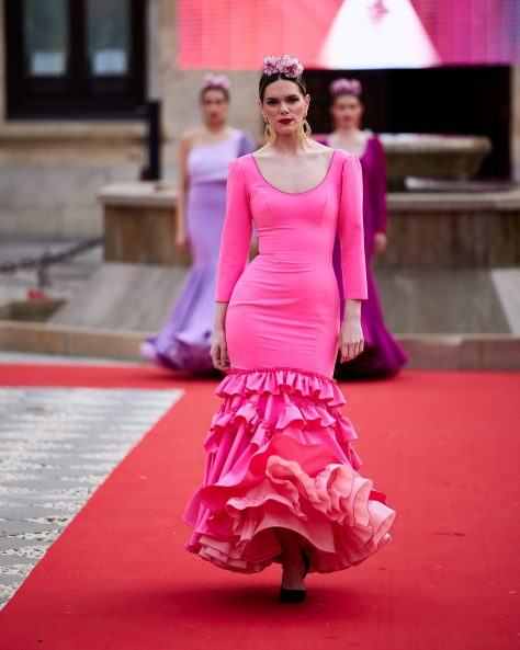 Vestido flamenca rosa chicle en tejido elástico, con manga lisa, escote delantero y trasero redondo y con volante grande en el bajo y volante pequeño como adorno