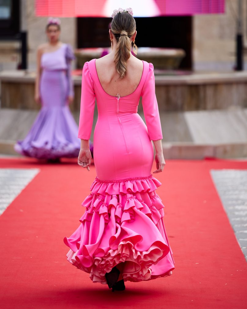 Vestido flamenca rosa chicle en tejido elástico, con manga lisa, escote delantero y trasero redondo y con volante grande en el bajo y volante pequeño como adorno