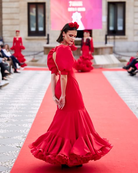 Vestido de flamenca rojo, mangas abullonadas, escote cerrado delantero y abierto en forma triangulo trasero. Volantes grande con mucho volumen y enaguas de rizo en rojo. Detalle encaje en espalda