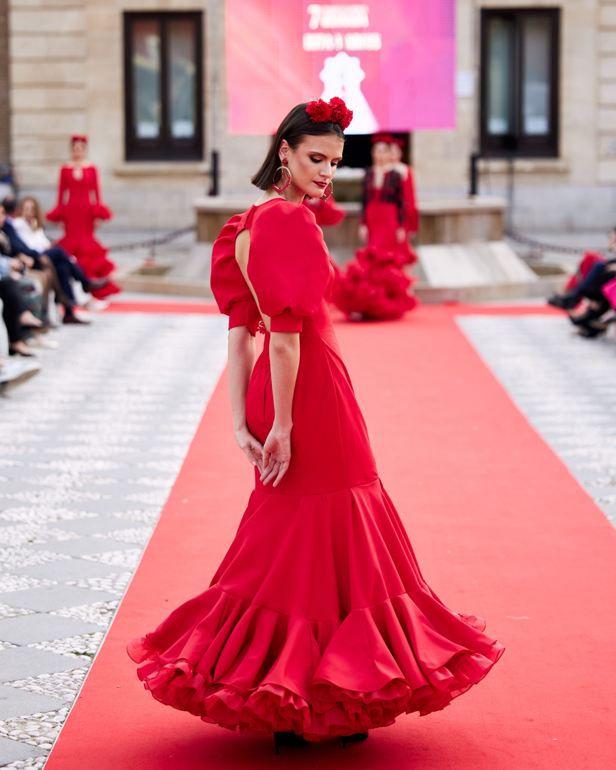 Vestido de flamenca rojo, mangas abullonadas, escote cerrado delantero y abierto en forma triangulo trasero. Volantes grande con mucho volumen y enaguas de rizo en rojo. Detalle encaje en espalda