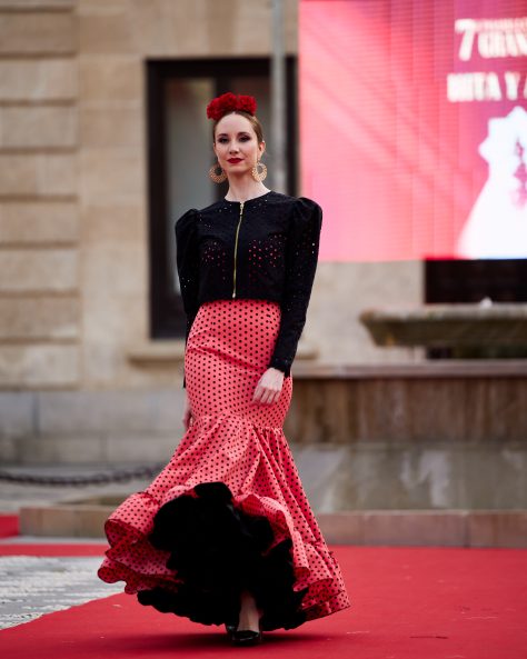 Vestido flamenca coral con lunar negro, escote delantero y trasero en redondo amplio y sin mangas. Volante amplio enganchado a otro volante de rizo en el bajo, enagua de tana