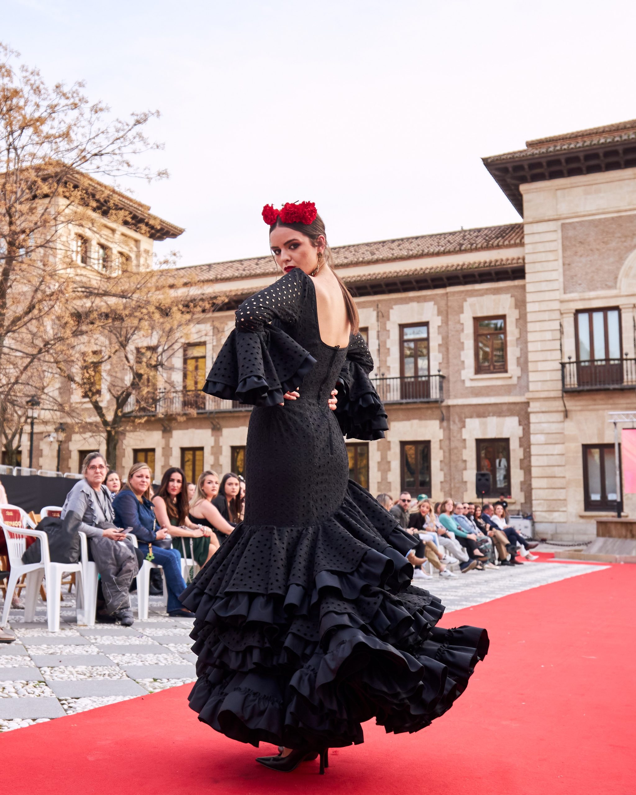 Vestido flamenca en tejido negro perforado con escote delantero y trasero cuadrado y adorno en el delantero, con tres volantes con rizo y manga larga con volante