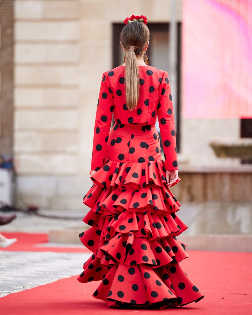 Vestido flamenca rojo con lunar negro con cinco volantes amplios encarados, sin mangas con escote en v muy pronunciado en el delantero y espalda