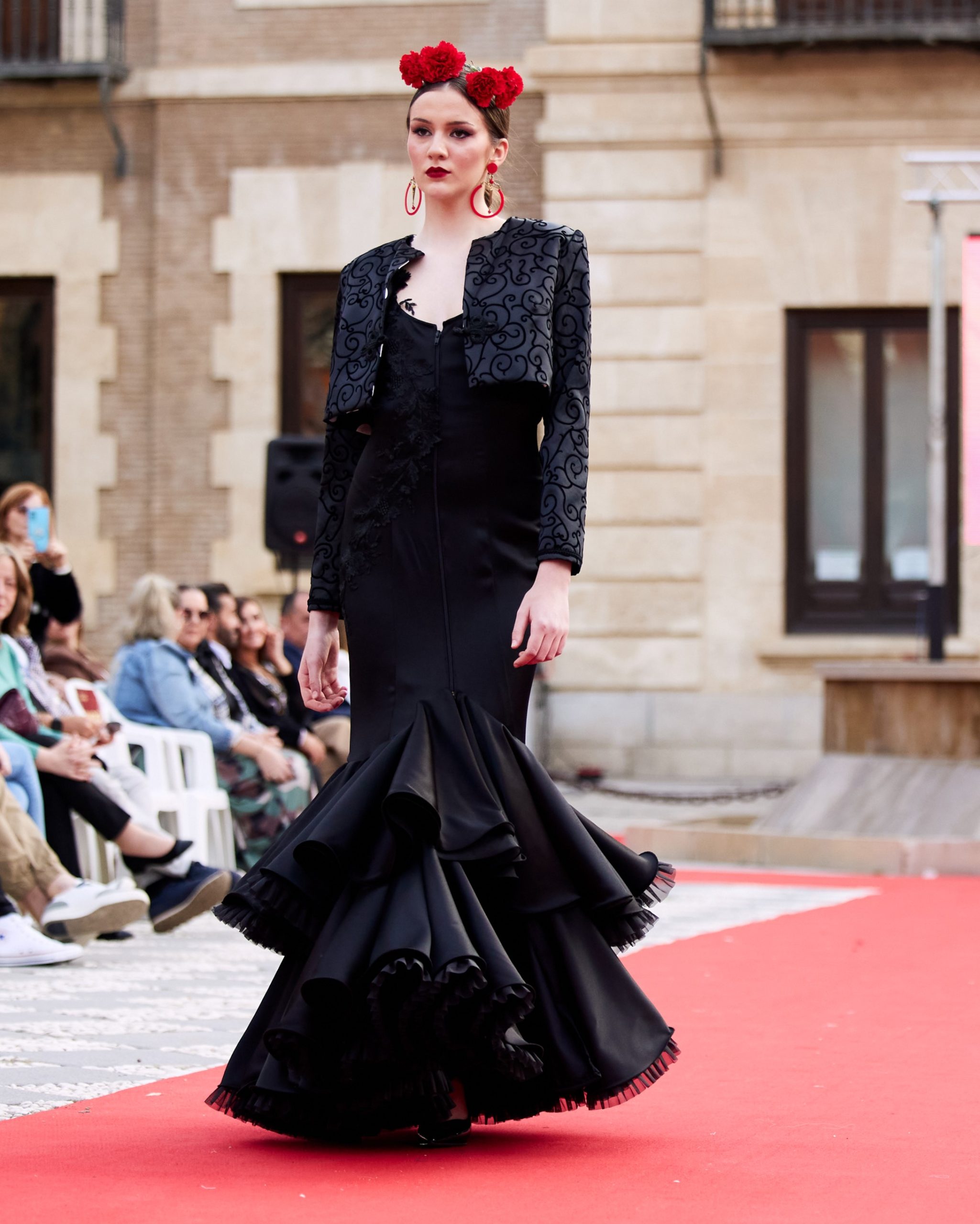 Vestido flamenca en tejido negro satinado con escote redondo por delante y por la espalda profundo, sin mangas con encaje como tirante y adorno en el cuerpo, con dos volantes grandes