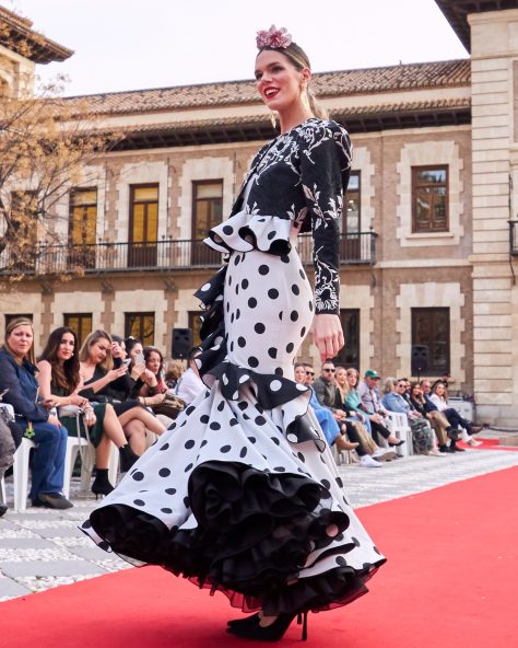 Vestido flamenca gris con lunar en negro, escote corazón con tirante de pasamanería, adorno de volante estilo péplum y con caída sobre la falda, volante grande en el bajo con enagua con vuelo.