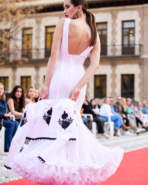 Vestido blanco en tejido perforado con un volante grande con volantito, sin mangas con escote delantero y trasero en pico profundo. Enagua de clavel en blanco muy voluminoso.